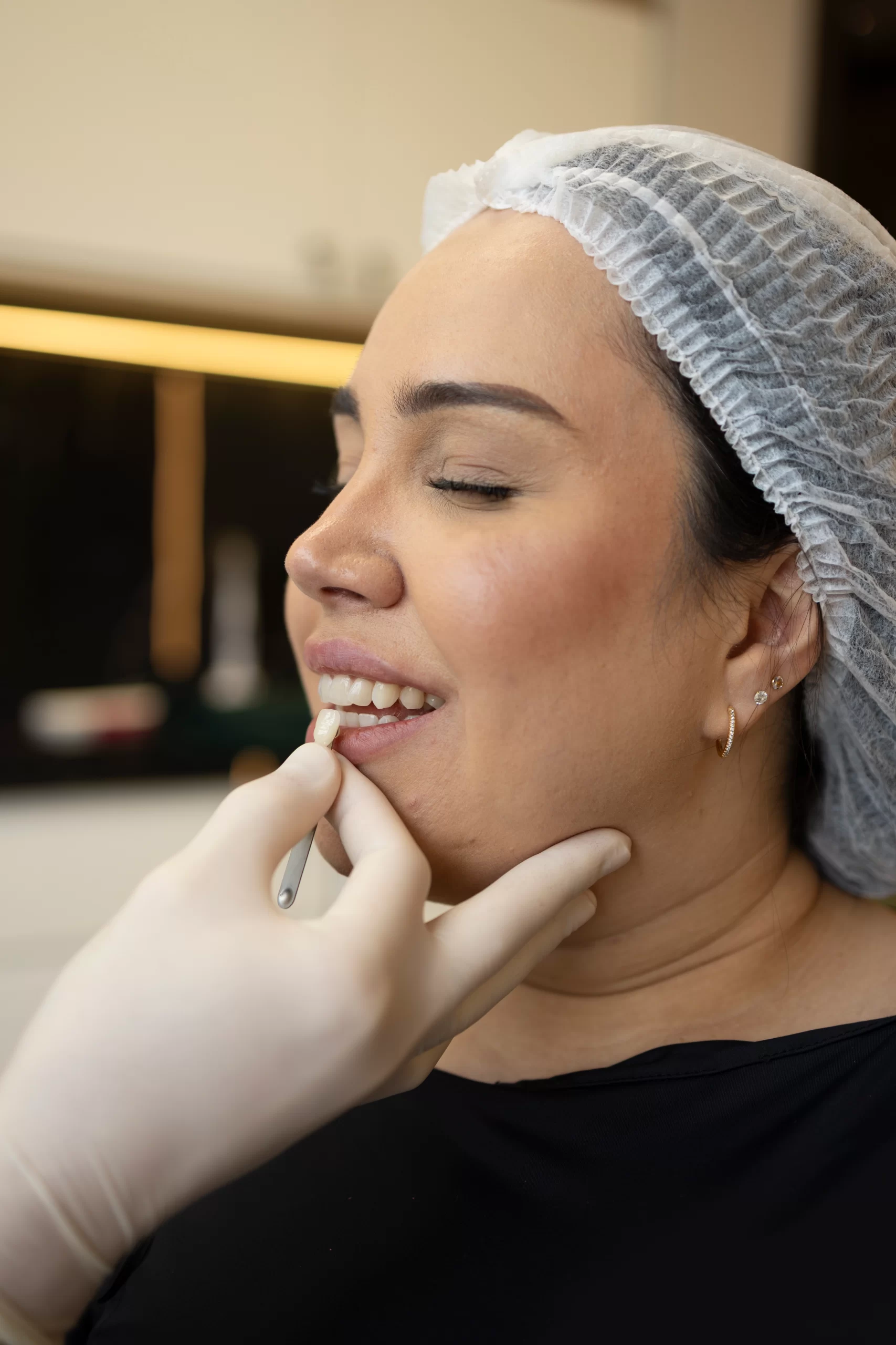 Uma profissional da clínica Eco Odontologia, utilizando luvas de proteção, realiza um procedimento minucioso de dentística estética para restaurar a harmonia do sorriso de uma paciente. Com o auxílio de uma escala de cores técnica, é feita a escolha precisa da tonalidade para garantir que restaurações, facetas ou recontornos estéticos se integrem perfeitamente aos dentes naturais. A imagem destaca o cuidado personalizado e o uso de materiais de alta qualidade no Eco Medical Center, em Curitiba, focando em devolver não apenas a beleza e a autoestima, mas também a saúde e a funcionalidade duradoura de cada elemento dental com máxima naturalidade.