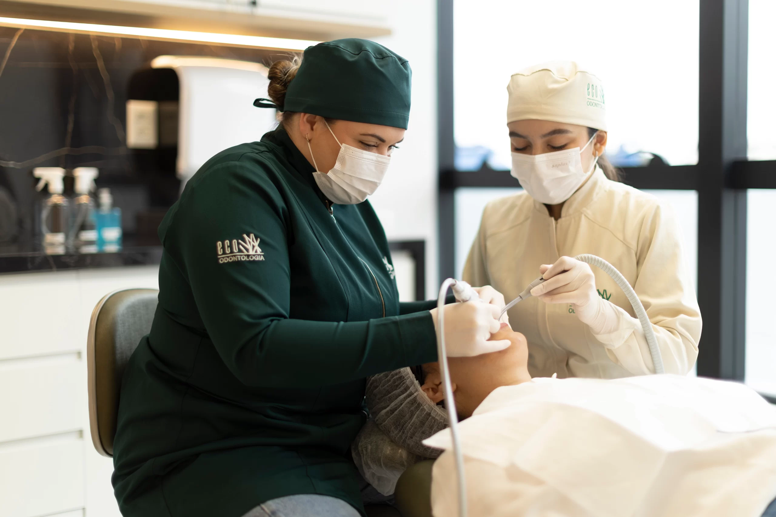 Em um ambiente de consulta acolhedor e profissional na clínica Eco Odontologia, uma dentista conversa de forma sorridente e empática com uma paciente. Ambas estão sentadas em uma moderna sala de atendimento clínico-geral, equipada com notebook para análise de casos e planejamento personalizado. A imagem destaca o foco da clínica no atendimento humanizado, na transparência do diálogo e no bem-estar do paciente, reforçando a excelência da Eco Odontologia em oferecer uma experiência odontológica segura, confortável e de alto padrão desde a primeira avaliação.