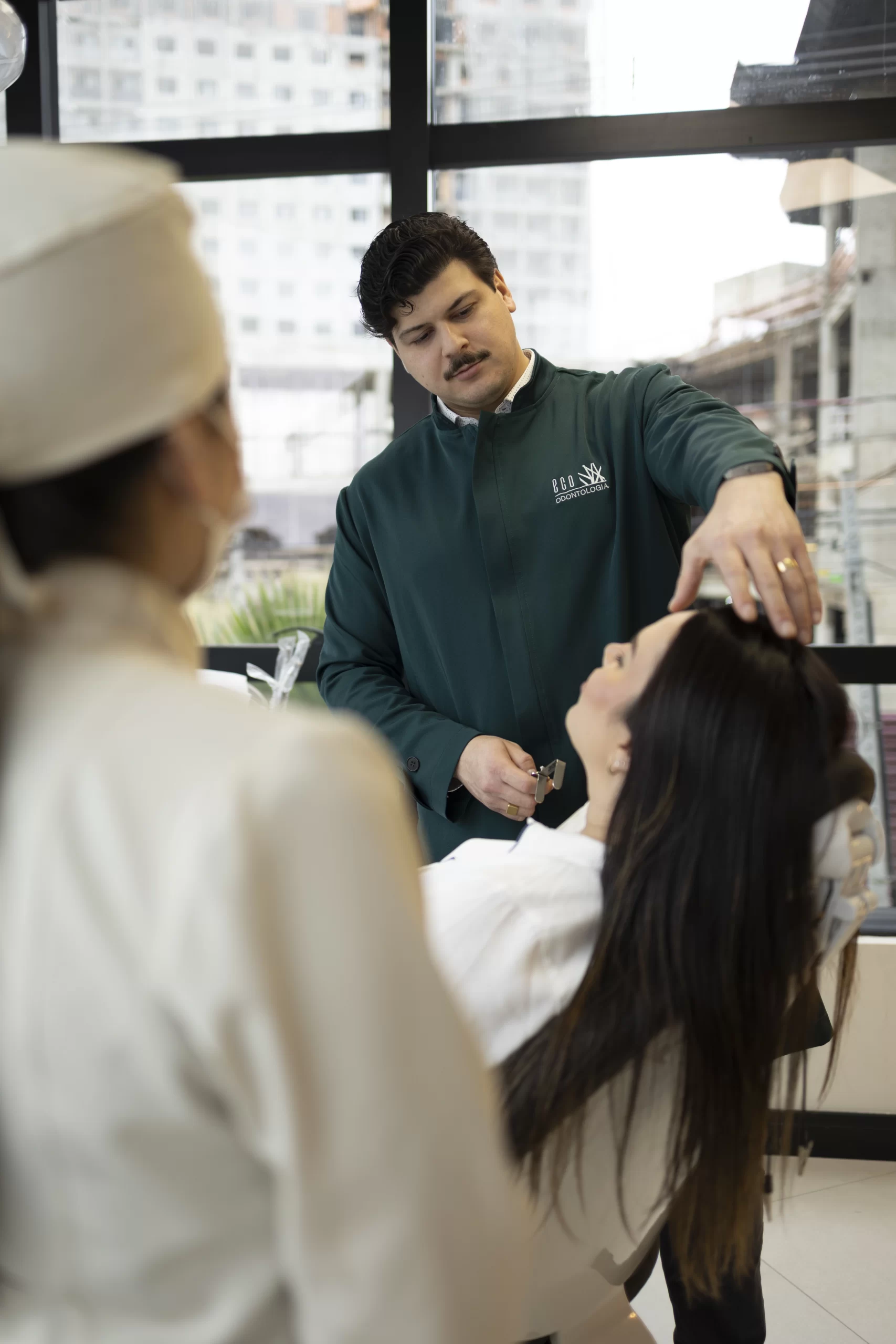 Na clínica Eco Odontologia, um cirurgião especializado realiza uma avaliação minuciosa em uma paciente para o tratamento de traumatologia bucomaxilofacial. O profissional utiliza técnicas avançadas para analisar a estrutura facial e dentária, focando na restauração da função e da estética após impactos ou acidentes. A cena, capturada em um consultório moderno no Eco Medical Center em Curitiba, destaca o uso de tecnologia de ponta e o atendimento humanizado necessários para tratar lesões e fraturas com precisão. A imagem reforça o compromisso da clínica em devolver a segurança e o bem-estar ao paciente através de diagnósticos modernos e um acompanhamento cuidadoso em todas as etapas da recuperação facial.