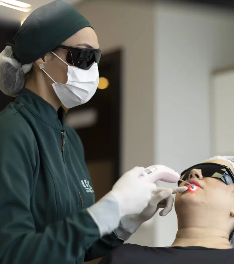 Na clínica Eco Odontologia, uma dentista especializada realiza um procedimento com tecnologia a laser em uma paciente deitada confortavelmente na cadeira odontológica. Ambas utilizam óculos de proteção específicos para o tratamento, evidenciando o rigoroso padrão de segurança e cuidado da clínica. A imagem destaca a aplicação de tratamentos modernos, indolores e altamente eficientes, reforçando o compromisso da equipe com o bem-estar, a inovação e a excelência nos serviços estéticos e terapêuticos de saúde bucal.