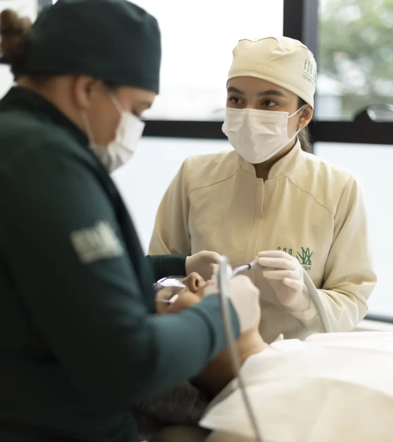 Duas profissionais especializadas da clínica Eco Odontologia realizam um procedimento odontológico em conjunto, demonstrando o trabalho em equipe e o alto padrão de cuidado com o paciente. A cena, capturada em um consultório moderno e iluminado, destaca o uso de equipamentos de precisão e o rigoroso seguimento de protocolos de segurança e higiene. A imagem enaltece o compromisso da clínica com um atendimento técnico de excelência e a atenção minuciosa dedicada a cada detalhe do tratamento para garantir a saúde e o bem-estar dos pacientes.